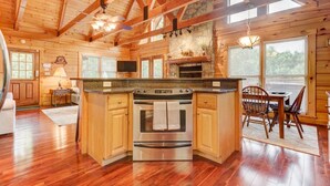 Una cocina amplia con isla central, vigas de madera, chimenea de piedra y ventanas grandes.