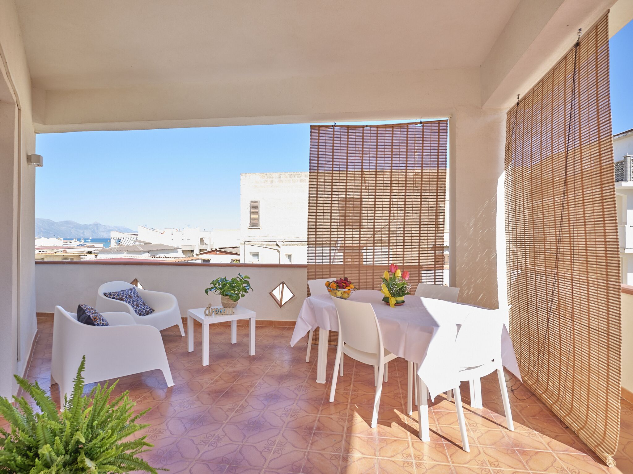A balcony with white furniture, a tiled floor, and a view of buildings and mountains.