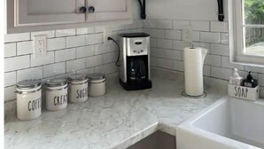 Une cuisine avec des meubles blancs, une machine à café et des bocaux étiquetés pour le café, la crème et le sucre.