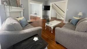 Un salon avec deux canapés gris, une table basse blanche, une cheminée et un escalier menant à une autre pièce.