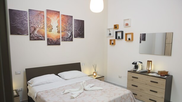 Un dormitorio ordenado con cama, mesitas de noche, cómoda y cuadros en la pared.