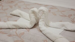 Una toalla blanca doblada en forma de corazón sobre una cama con estampado floral.