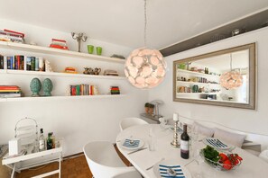 A dining area with a white table set for four, a hanging light fixture, and shelves with books and decorative items. - Feeling Home Lugano (Canobbio)