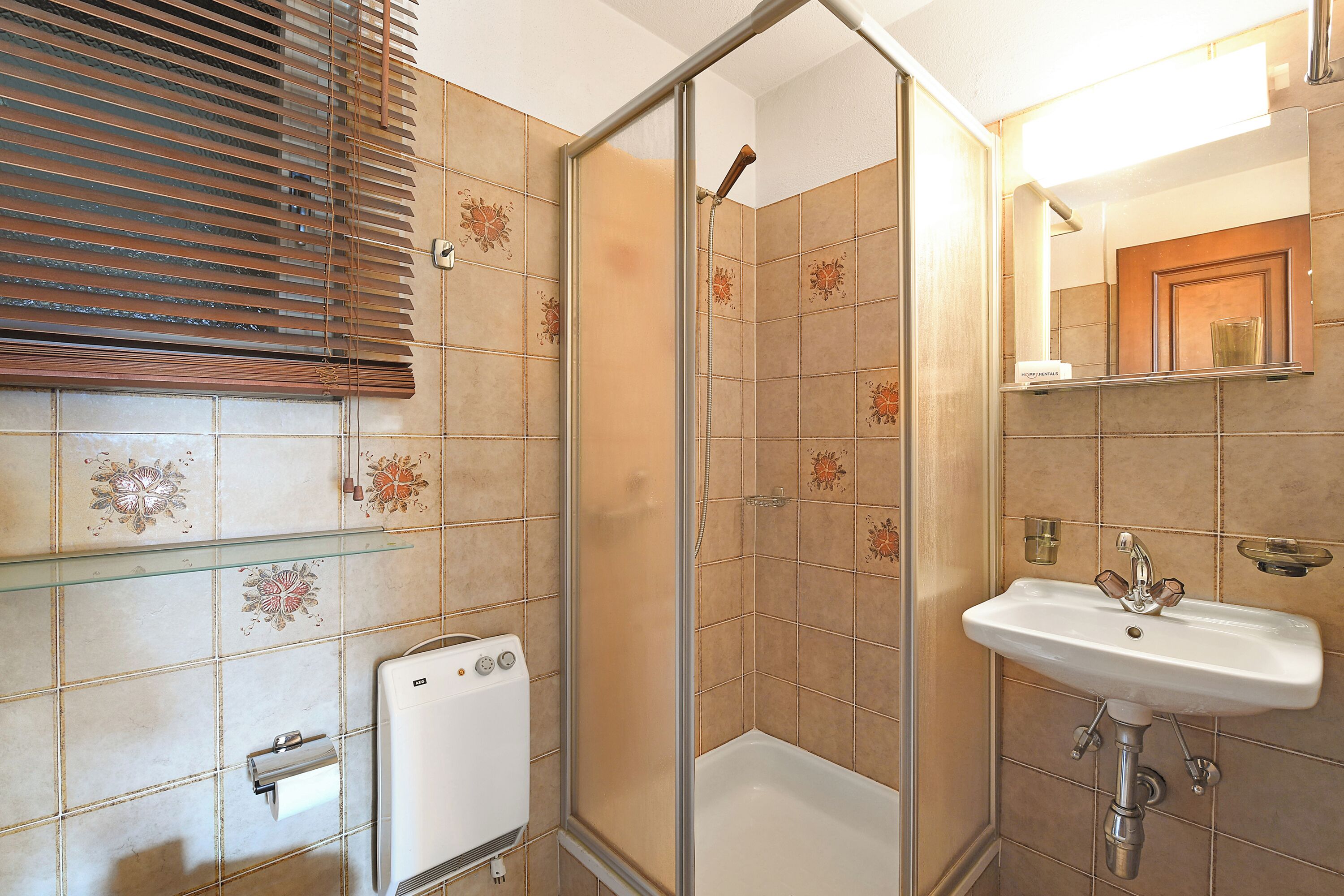 A bathroom with a glass shower enclosure, a white sink, and a towel dispenser.