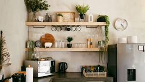 Una cocina con un estante de madera que sostiene plantas, un reloj y cristalería.