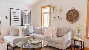 A modern living room with a sectional sofa, a glass coffee table, and a small side table with a vase. - Doma Lodge - Cozy Muskoka Cabin in the Woods (Huntsville)