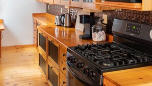 A kitchen with wooden cabinets, a microwave, a stove, and a coffee maker. - Doma Lodge - Cozy Muskoka Cabin in the Woods (Huntsville)