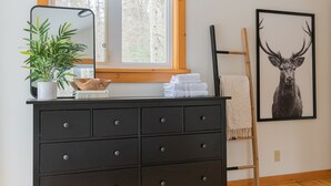 A dark wooden dresser with multiple drawers, a potted plant, and a framed deer picture on the wall. - Doma Lodge - Cozy Muskoka Cabin in the Woods (Huntsville)
