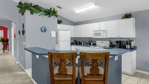 A modern kitchen with white cabinets, a blue island, and two wooden chairs with pineapple designs. - Home in Davenport close to Parks w/Pool (Davenport)