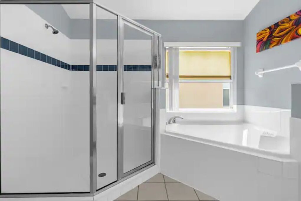 A modern bathroom with a glass-enclosed shower, a window, and a white bathtub.