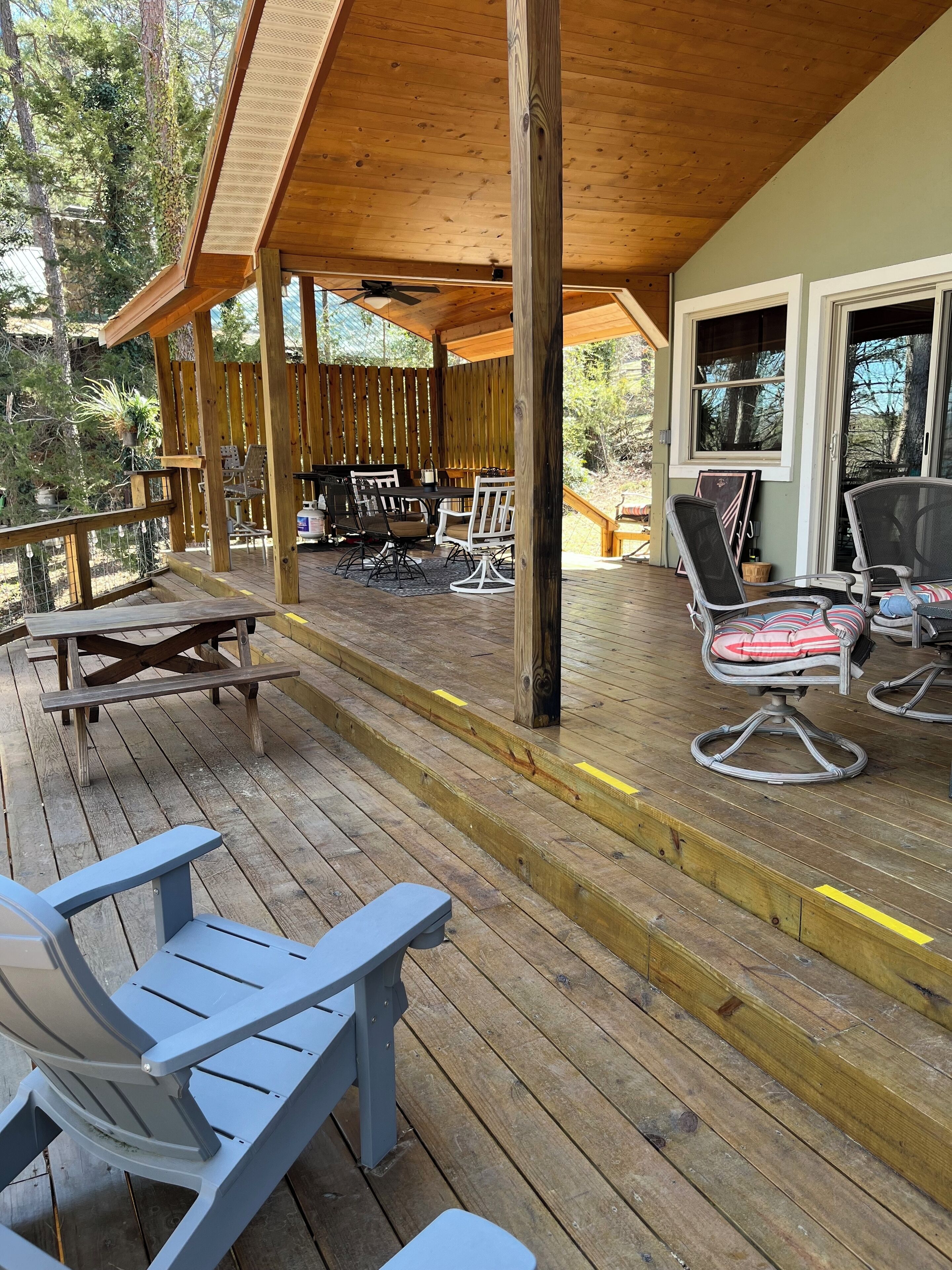 A wooden deck with outdoor seating, including chairs and tables, and a covered area with a ceiling fan.