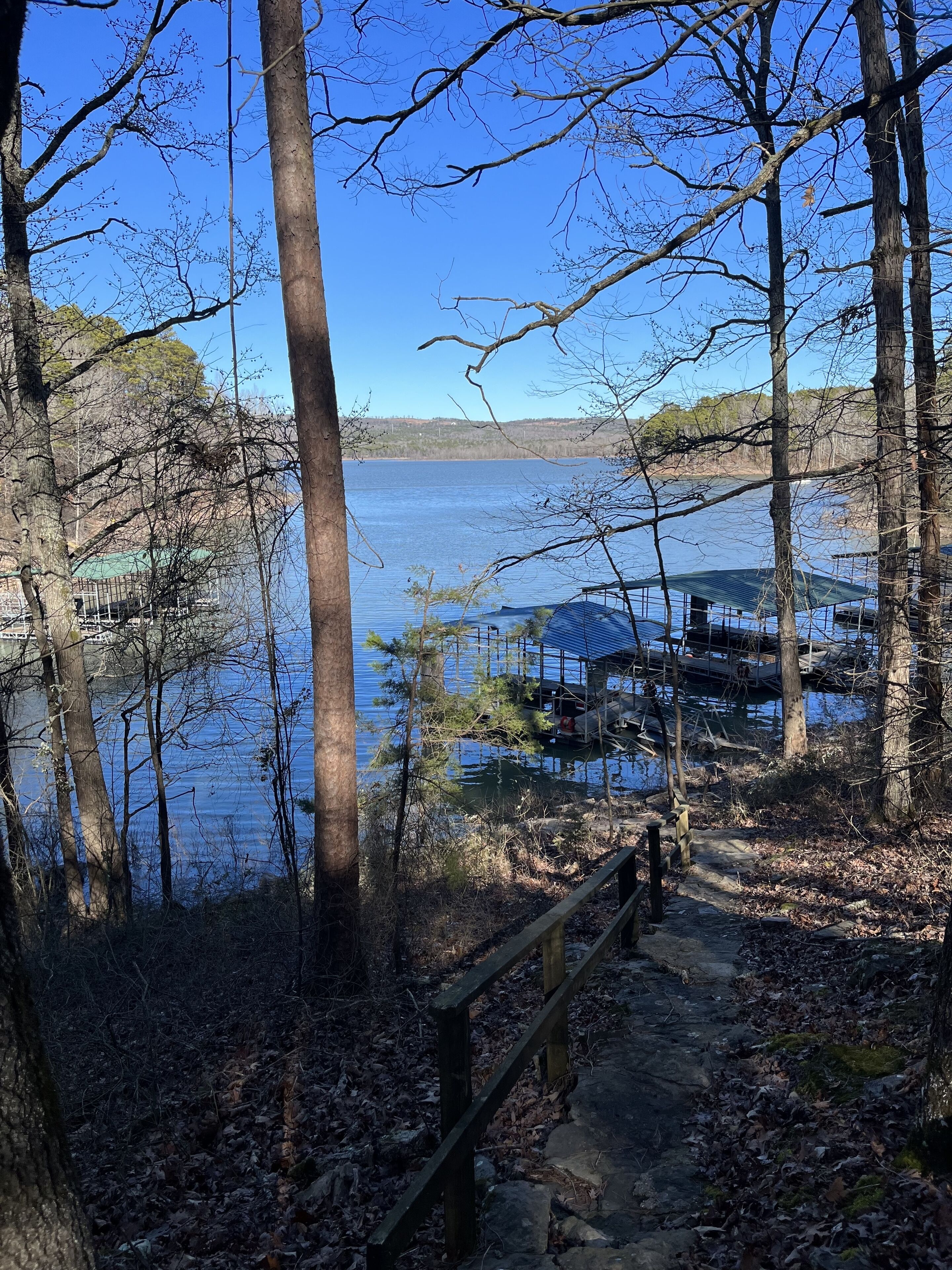 Une vue sur le lac, avec un quai, une passerelle en bois et des arbres tout autour.