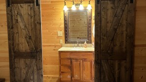 Una stanza rustica con pavimenti in legno, un letto, uno specchio grande con luci integrate e un armadietto in legno.