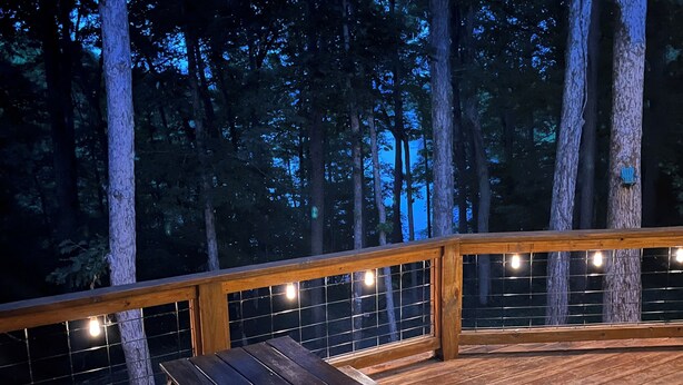 Un pontile in legno con tavolo da picnic, circondato da alberi alti e luci decorative.
