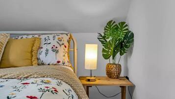 Un dormitori amb un llit, una tauleta de nit amb una làmpada i una planta gran.