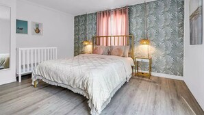 Une chambre à coucher avec un lit, deux tables de chevet, un mur orné d’un motif de feuilles et un radiateur blanc.