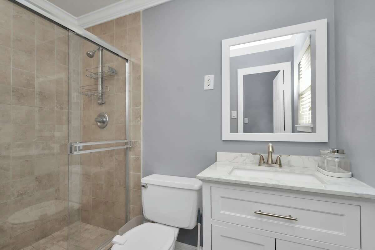 Une salle de bain avec une douche à parois de verre, des toilettes blanches, un lavabo en marbre et un grand miroir.