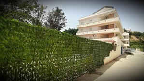 Un edificio de varios pisos con balcones, un camino de entrada con puerta de rejas y un seto verde.