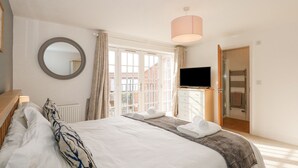 A hotel room with a bed, a TV, a mirror, and a window with curtains. - The Mill Stones (Norwich)