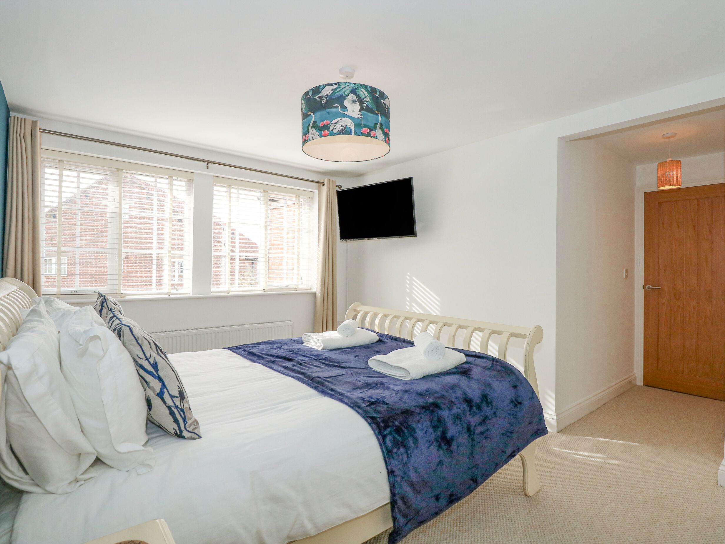 A bedroom with a bed, a TV mounted on the wall, and a window with blinds.