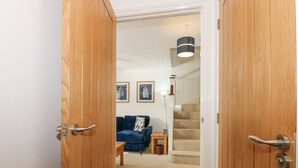 A room with a wooden door, a blue sofa, a small table, a lamp, and a staircase leading to another level. - The Mill Stones (Norwich)