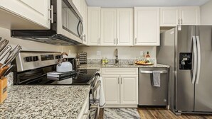 A modern kitchen with white cabinets, stainless steel appliances, and a granite countertop. - Little Treasure House minutes from Beach & Mercato (Naples)