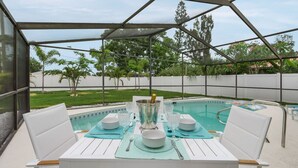 An outdoor patio with a pool, white chairs, and a table set for dining. - Little Treasure House minutes from Beach & Mercato (Naples)