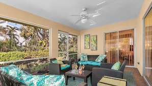 A sunlit patio with wicker furniture, a ceiling fan, and tropical artwork. - Tropical vacation home close to Vanderbilt Beach (Naples)