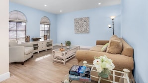 A living room with a beige sofa, a white armchair, a coffee table, and a bookshelf. - Tropical vacation home close to Vanderbilt Beach (Naples)