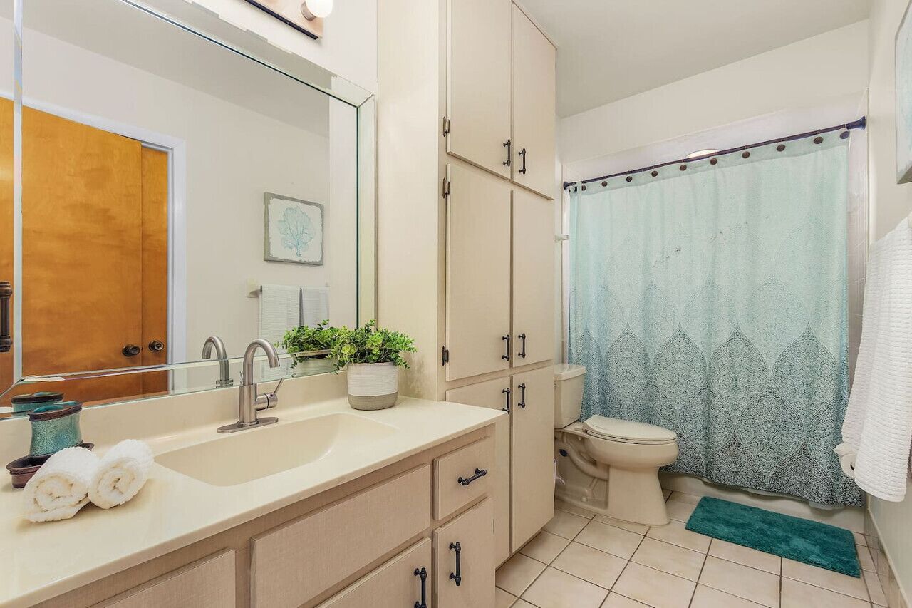Un bagno con lavandino, specchio, mobili, water e tenda doccia.