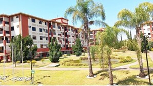 A multi-story hotel with balconies, a well-maintained garden with palm trees, and a clear sky. - Luxuoso Flat em Reort com vista incrível (Brasília)