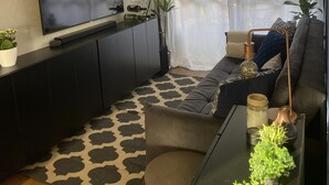 A modern living room with a flat-screen TV, dark furniture, a patterned rug, and several potted plants. - Luxuoso Flat em Reort com vista incrível (Brasília)