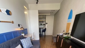 A modern living room with a grey sofa, wooden flooring, a TV, and a kitchen area in the background. - Luxuoso Flat em Reort com vista incrível (Brasília)