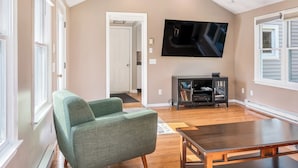 Een ruime woonkamer met een groene fauteuil, een houten eettafel en een flatscreen televisie aan de muur.