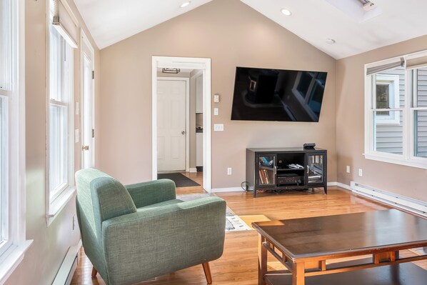 Un salón espacioso con un sillón verde, una mesa de comedor de madera y un televisor de pantalla plana montado en la pared.