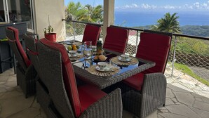 Ein Essbereich mit Korbstühlen und einem Tisch für zwei Personen, mit Blick auf eine malerische Aussicht auf das Meer und die Hügel.