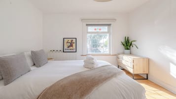 A bedroom with a bed, a radiator, a window with a view, a dresser, and a potted plant.