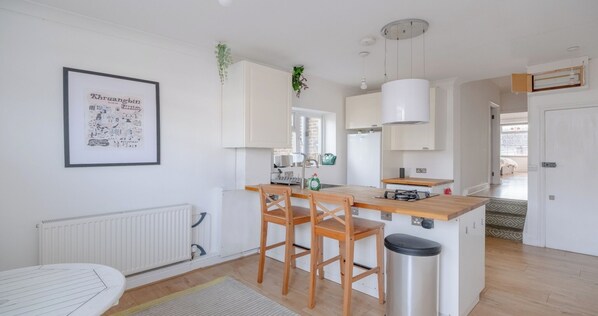 A modern kitchen with white cabinetry, a wooden island with bar stools, a hanging plant, and a framed picture on the wall.