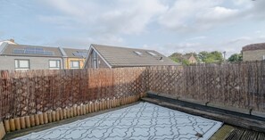 A backyard with a patterned mat, a wooden fence, and a house with solar panels.