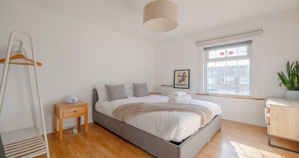 A bedroom with a bed, bedside table, lamp, radiator, window, and a plant.