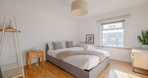 A bedroom with a bed, bedside table, lamp, radiator, window, and a plant.