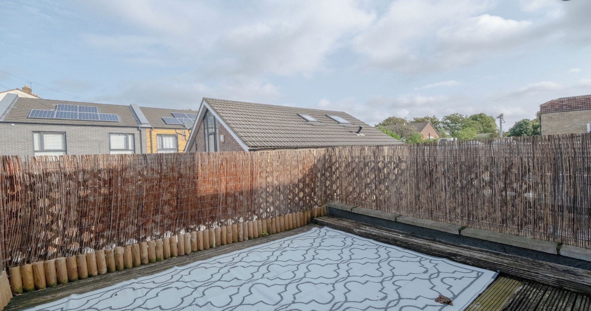 A backyard with a patterned mat, a wooden fence, and a house with solar panels.