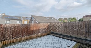 A backyard with a patterned mat, a wooden fence, and a house with solar panels.