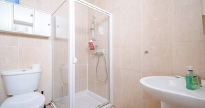 A bathroom with a toilet, a shower enclosure, and a sink with a soap dispenser.