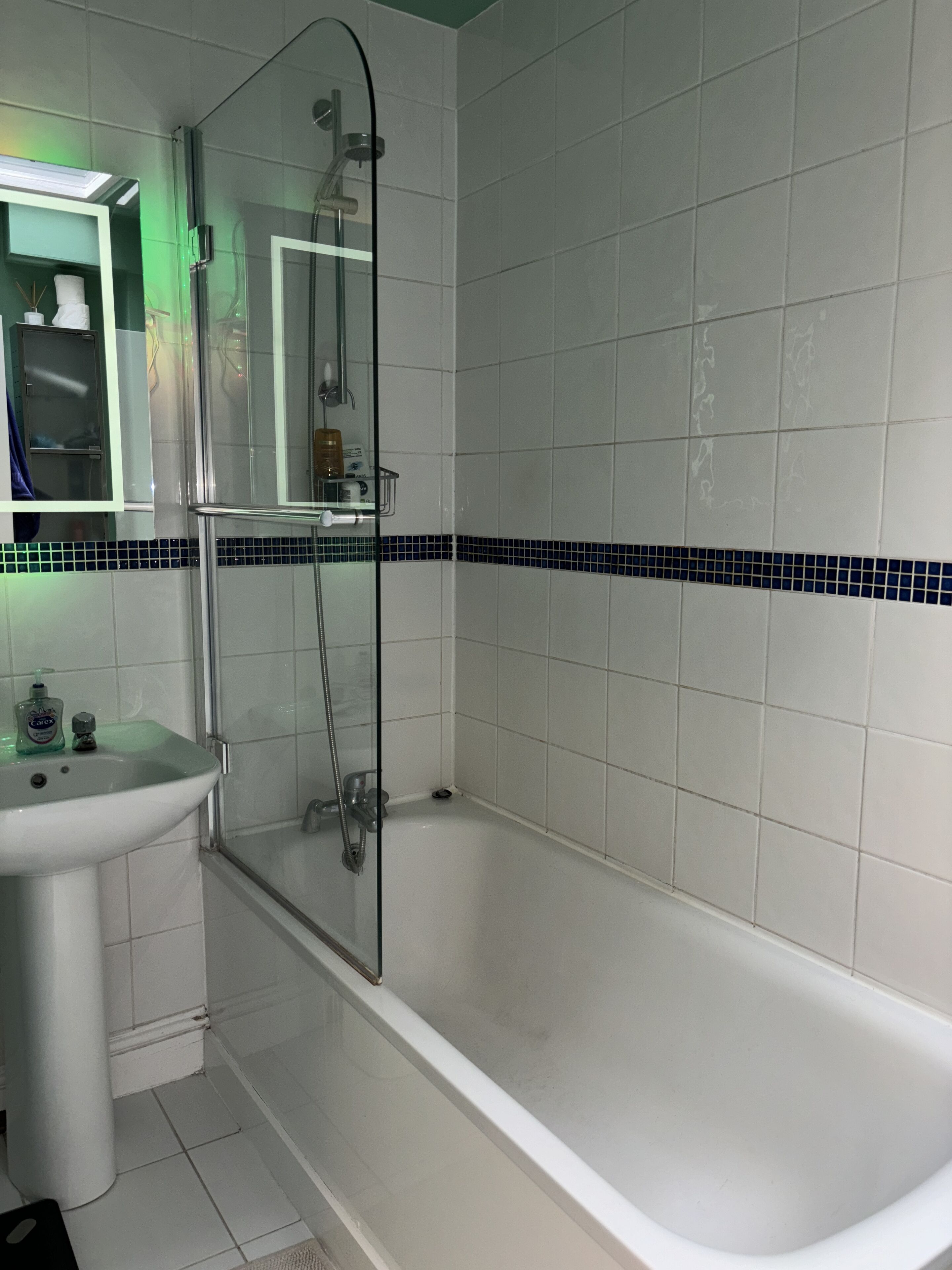 A bathroom with a white bathtub, a glass shower enclosure, a sink, and a mirror.