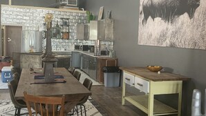 Een moderne keuken met een centraal eiland, een eetgedeelte met een houten tafel en stoelen, en een groot zwart-wit schilderij van een bizon aan de muur.