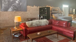 Een moderne woonkamer met een rode leren bank, een houten salontafel, een lamp en een boekenkast tegen een bakstenen muur.