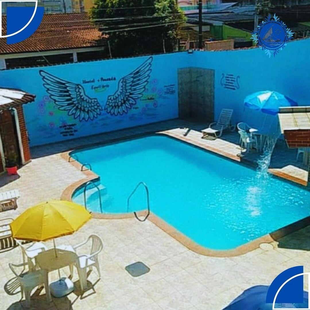 Una piscina con un mural de alas y una fuente, rodeada de sillas de descanso y un paraguas amarillo.