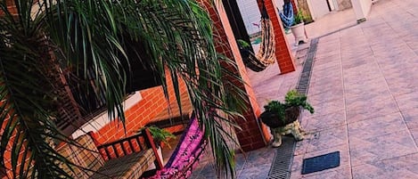 A courtyard with a hammock, potted plants, and a tiled floor.