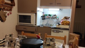 A compact kitchen with a microwave, stove, and sink. There are various kitchen items and decorations on the walls and counters.